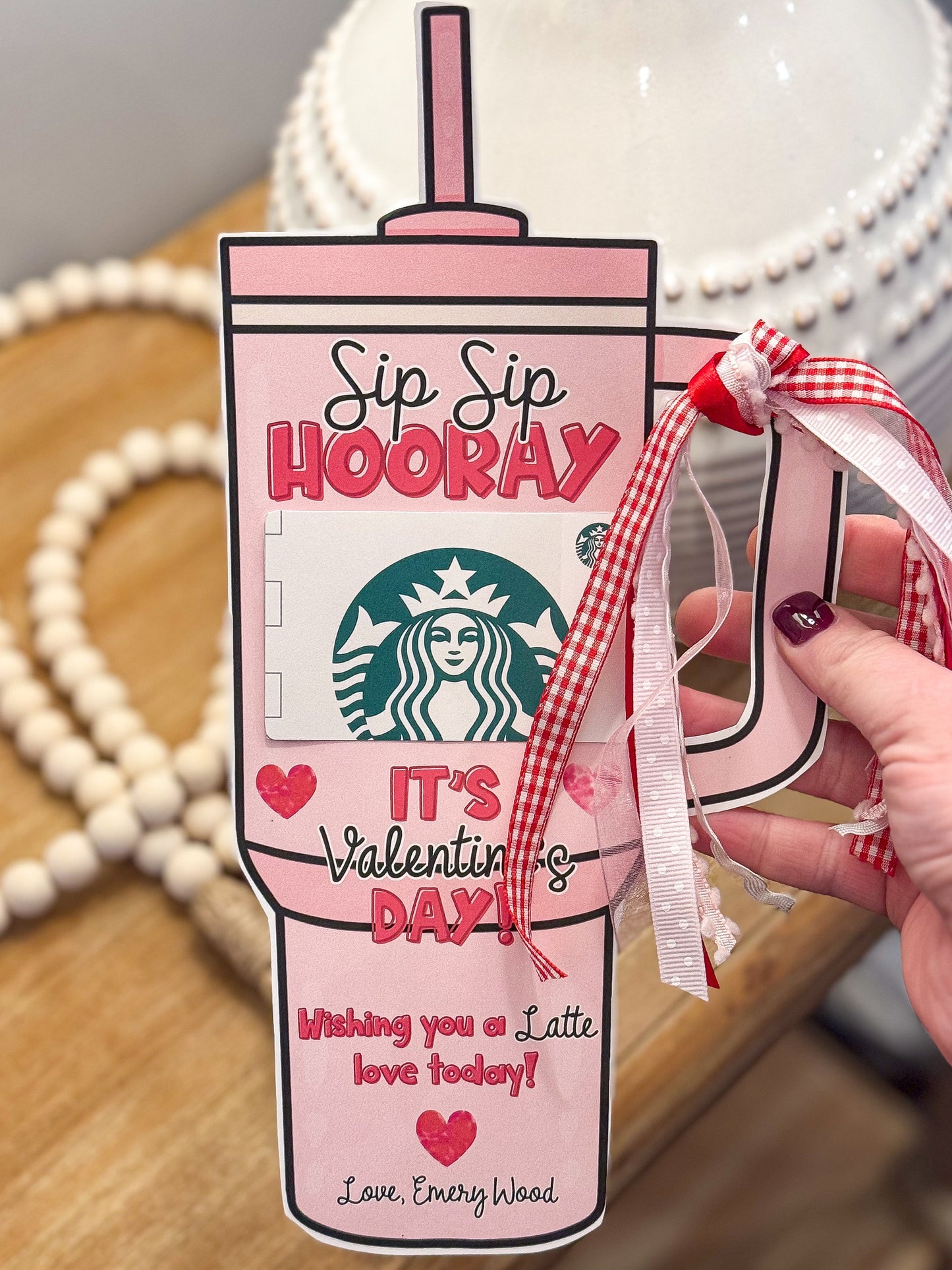 Valentine's Day themed Starbucks gift card holder with a straw and ribbon on a wooden surface.