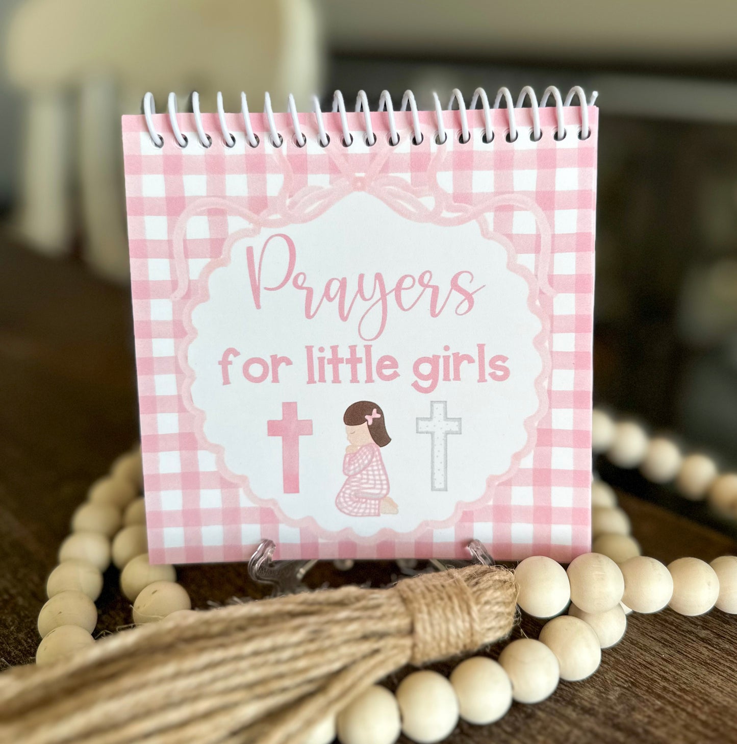 Small spiral-bound book titled 'Prayers for little girls' with a pink checkered design on a wooden surface.